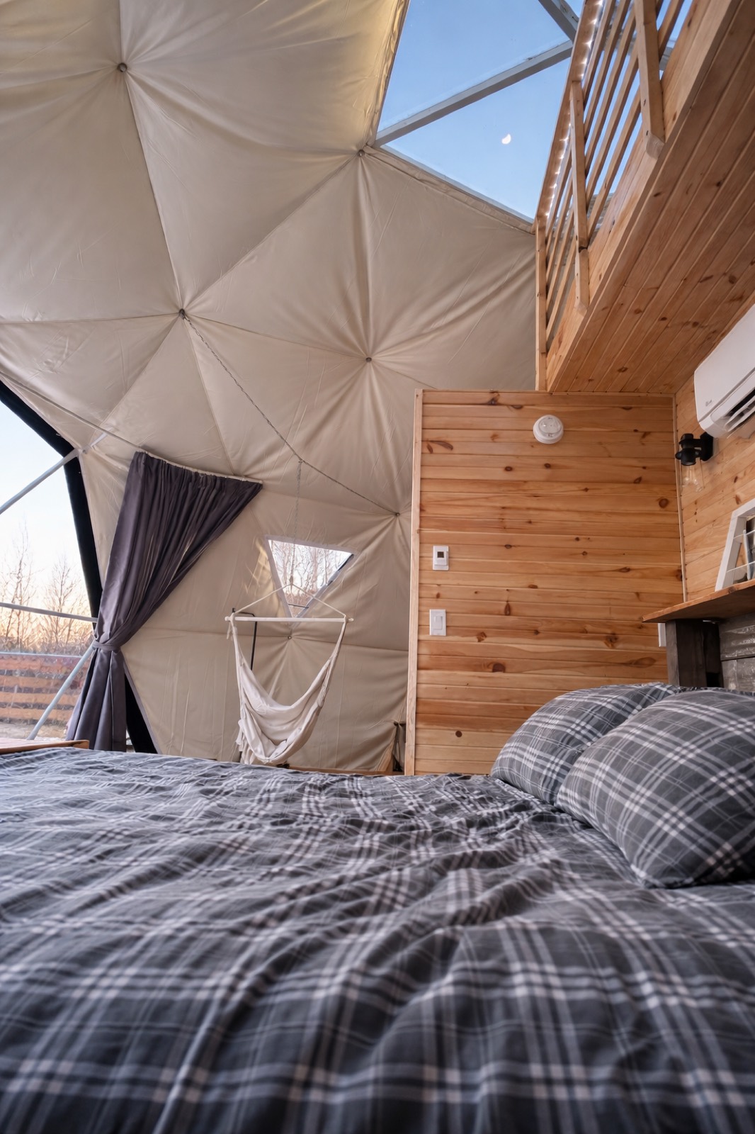 Hanging swing chair beside the bed inside a glamping dome
